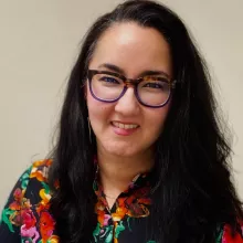 Leyla's headshot image appears here, she has long black hair, is wearing glasses and a colorful, floral blouse.