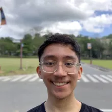 John smiling wearing clear plastic framed glasses behind clouds