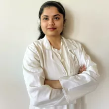 Zuha standing with her arms crossed in her lab coat with a white background