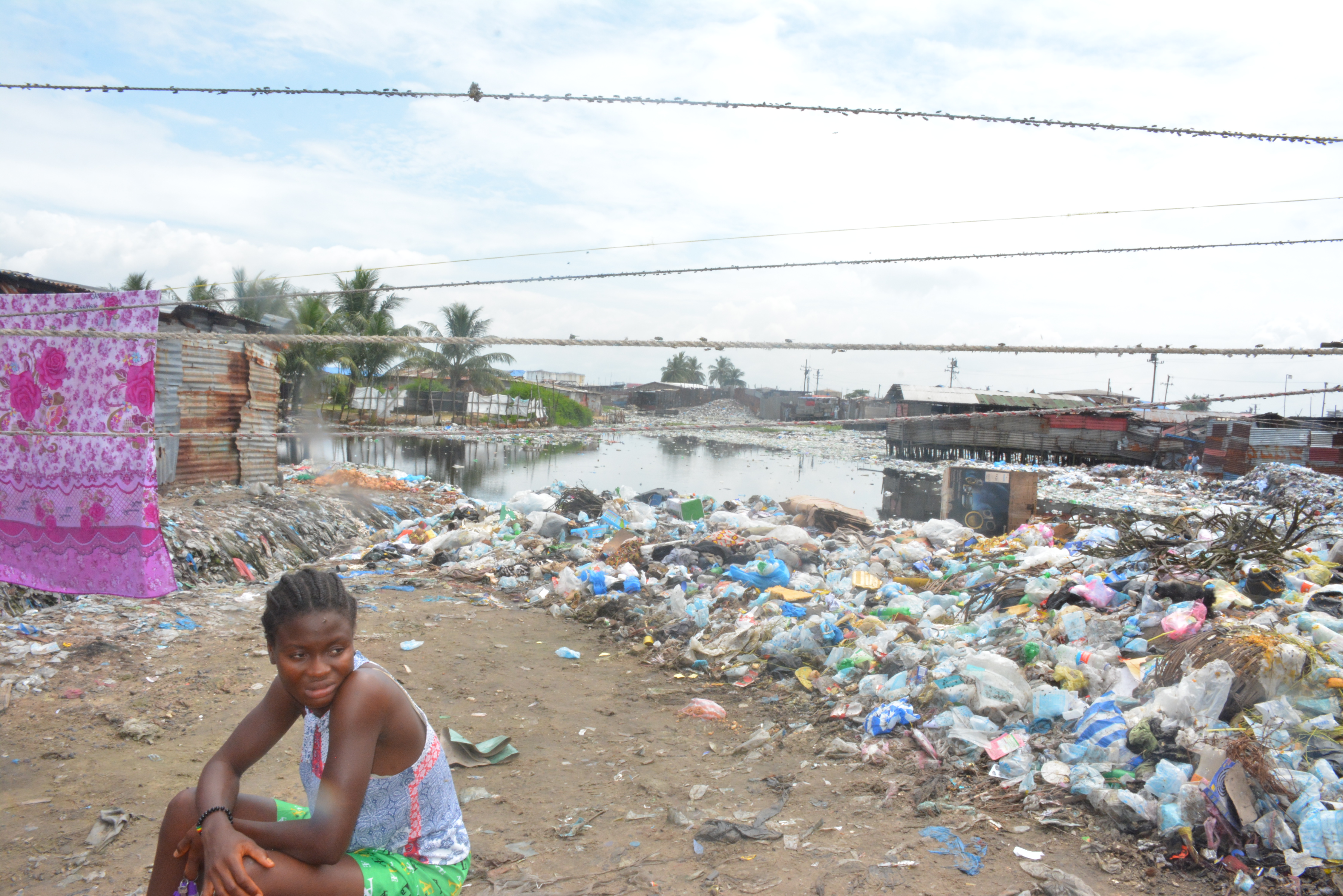 A girl at the West Point neighbourhood in Monrovia is seated with mounds of garbage behind her